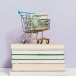 A small shopping cart with dollar bills placed on a stack of books, symbolizing financial literacy.
