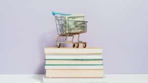 A small shopping cart with dollar bills placed on a stack of books, symbolizing financial literacy.