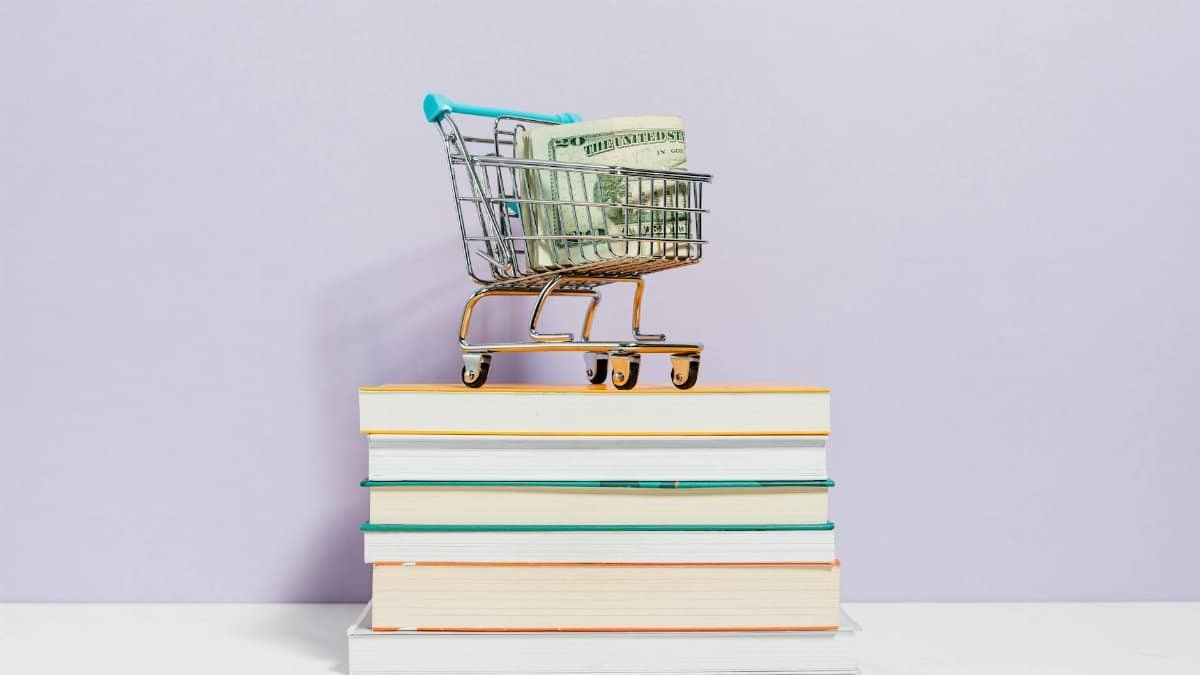 A small shopping cart with dollar bills placed on a stack of books, symbolizing financial literacy.