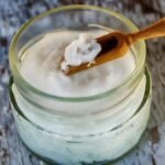 Close-up of organic coconut oil in glass jar with wooden spoon, perfect for natural health and wellness use.