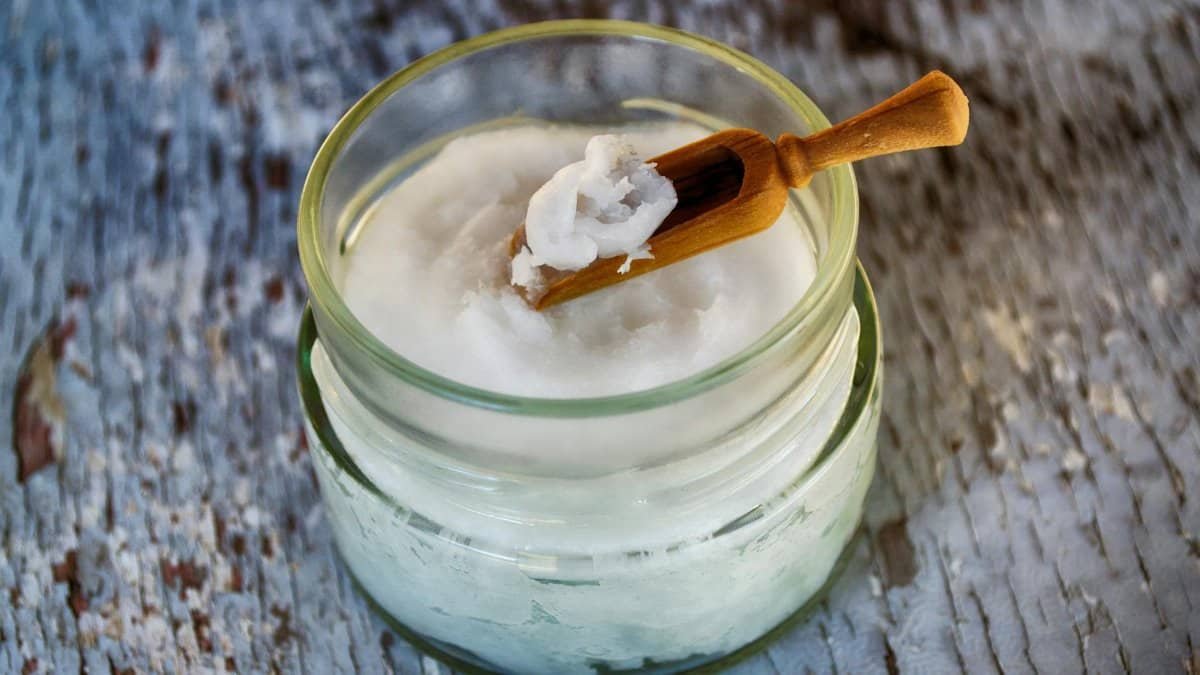 Close-up of organic coconut oil in glass jar with wooden spoon, perfect for natural health and wellness use.