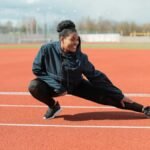 A woman in activewear stretches on a red running track outdoors, preparing for a workout.