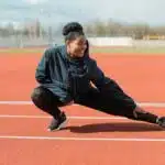 A woman in activewear stretches on a red running track outdoors, preparing for a workout.