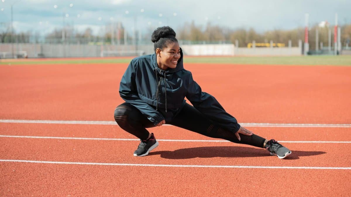 A woman in activewear stretches on a red running track outdoors, preparing for a workout.