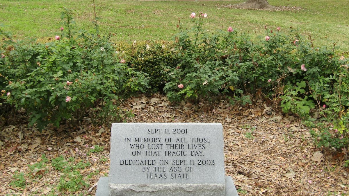 Memorial stone for 9/11 victims surrounded by roses in a peaceful park.