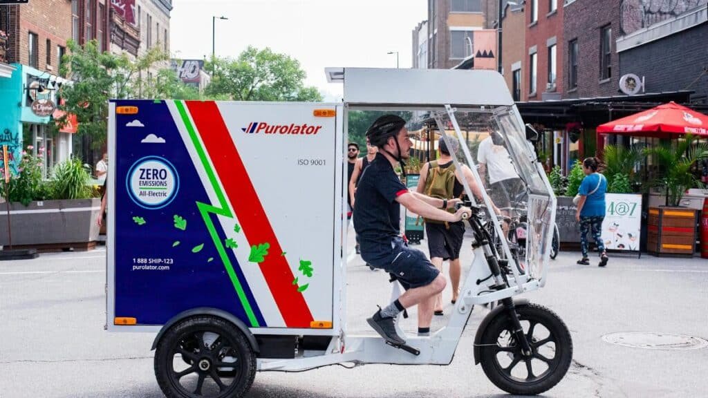 Side view of an electric delivery tricycle operated by a courier in an urban setting, promoting sustainable transit.