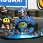Two racers navigate a sharp turn in a competitive go-kart race on an outdoor circuit.