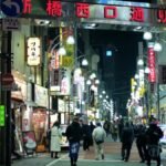 Bustling night scene in Minato City, Tokyo with people, shops, and illuminated street signs.