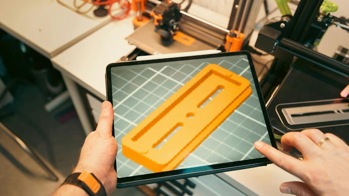 A person uses a tablet to view a 3D model prototype in a workshop equipped with 3D printers.