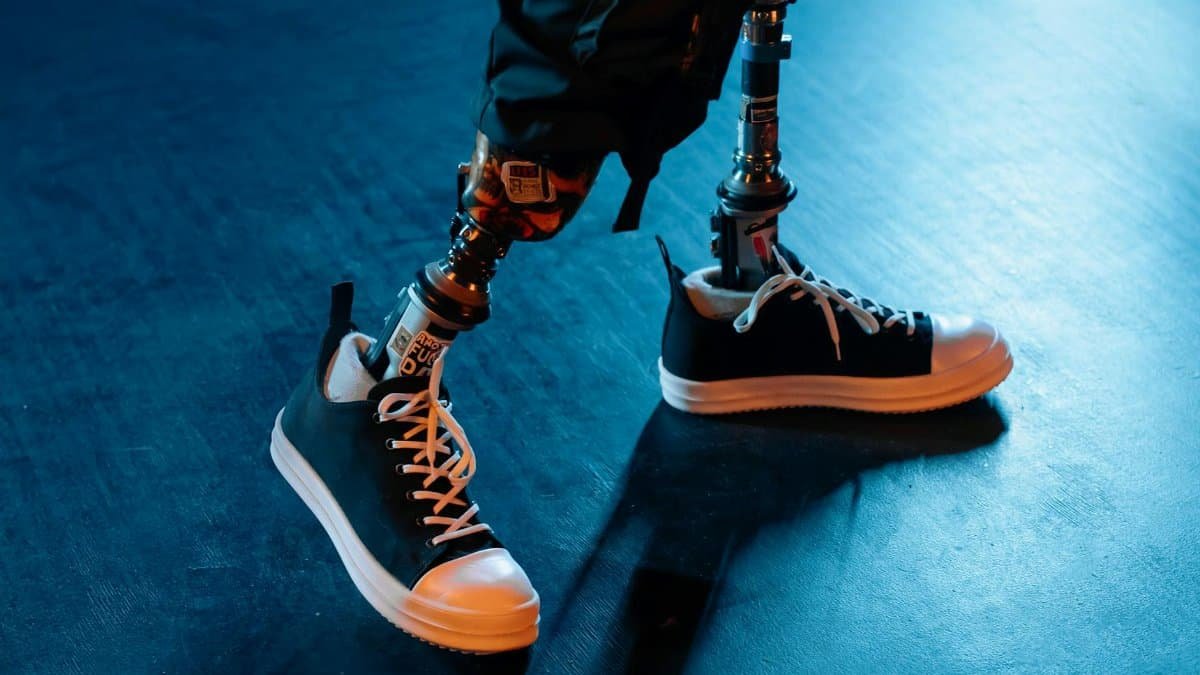 Close-up of prosthetic legs with black sneakers on a blue concrete floor in artificial lighting.