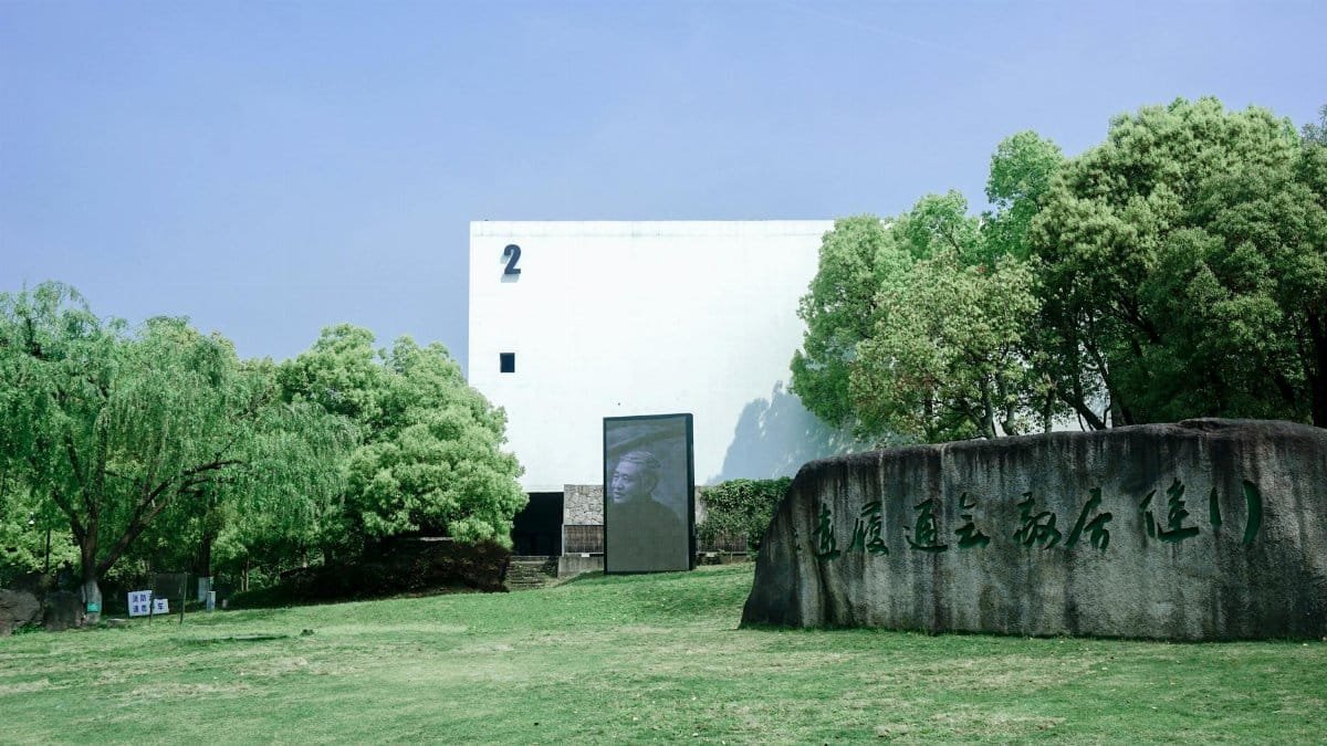 A modern museum building with a stone tablet, surrounded by lush greenery and clear sky.