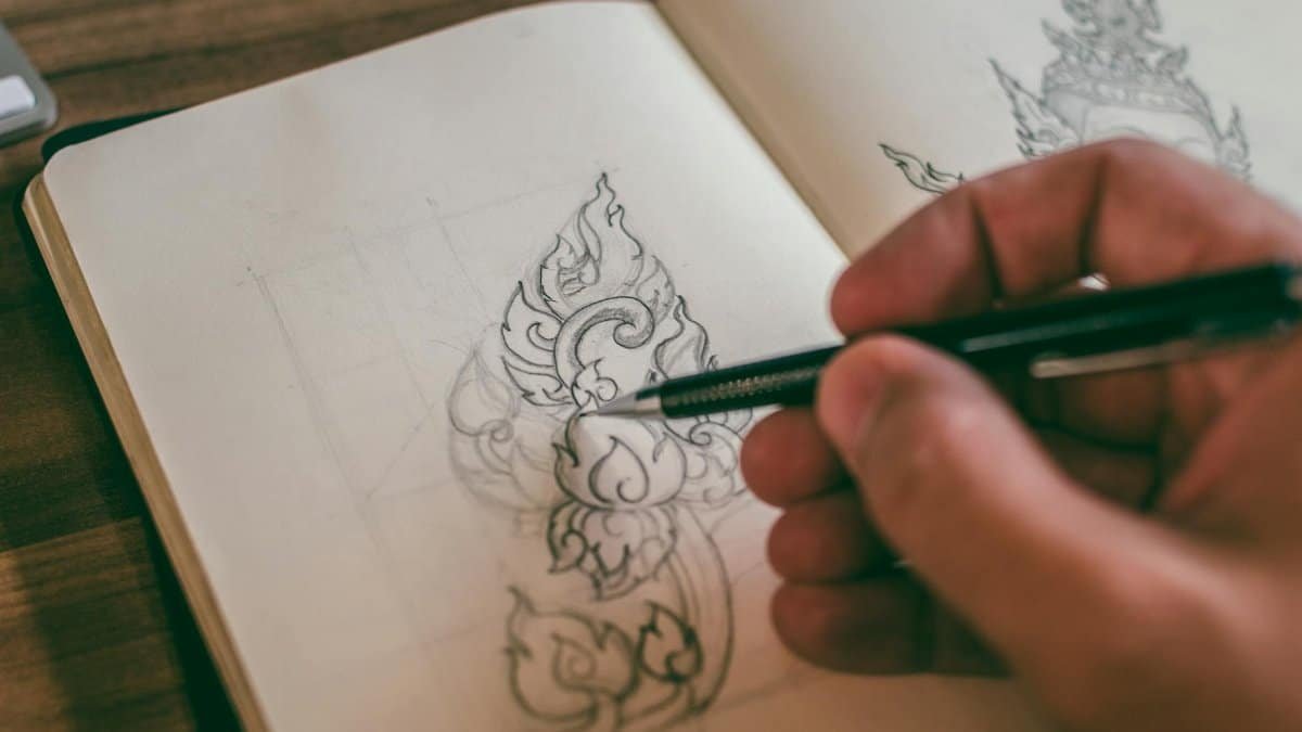 Close-up of a hand sketching detailed design in a sketchbook with mechanical pencil.