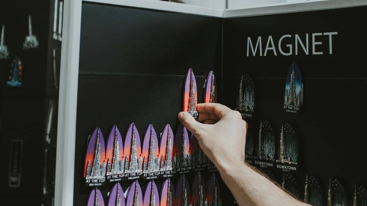A hand selecting colorful Burj Khalifa souvenir magnets from a display in Dubai shop.