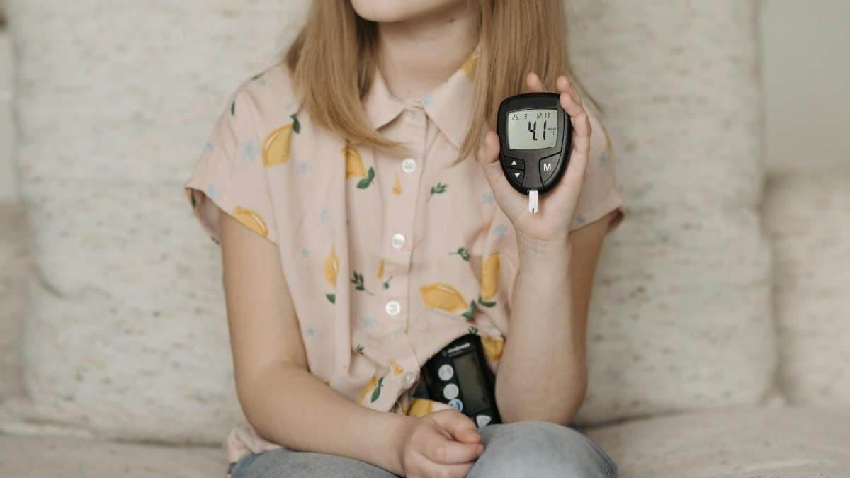 A young girl sitting at home using a glucometer to monitor her blood sugar levels, illustrating diabetes management.