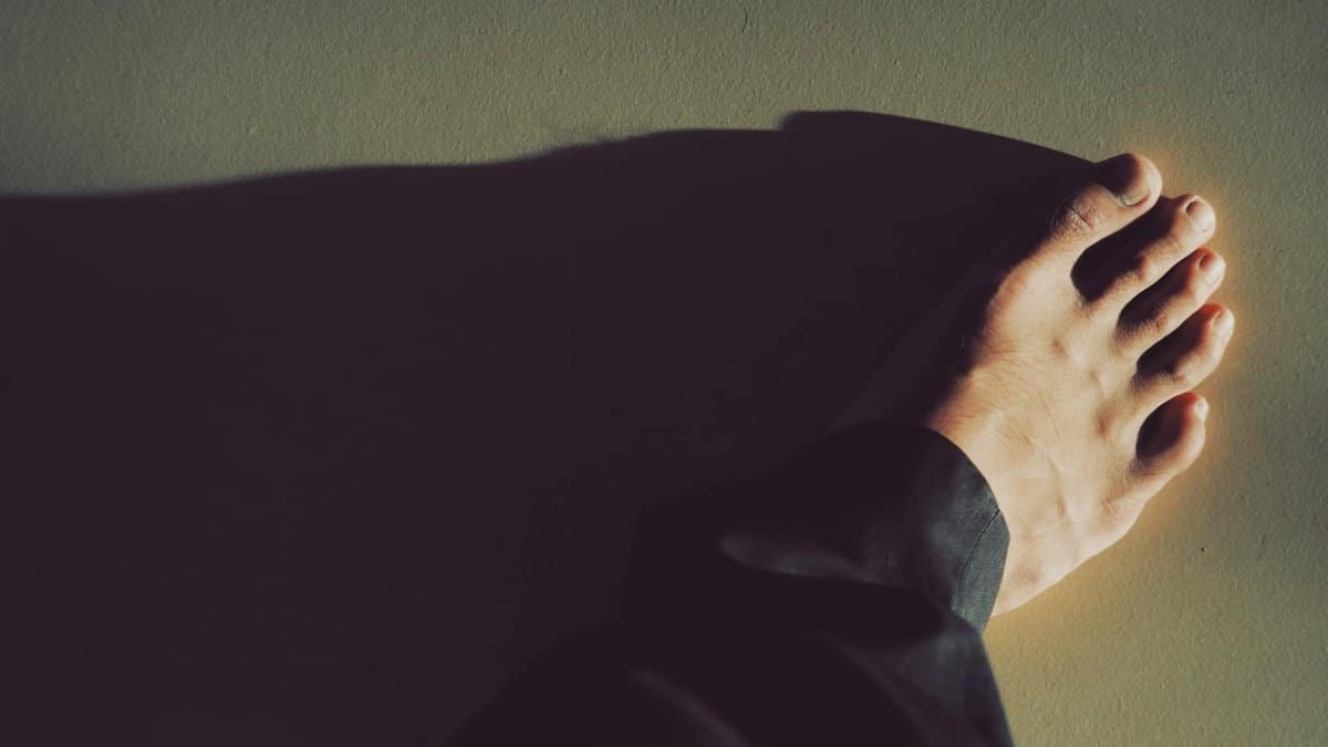 A close-up photo capturing a bare foot casting a dramatic shadow on the ground.