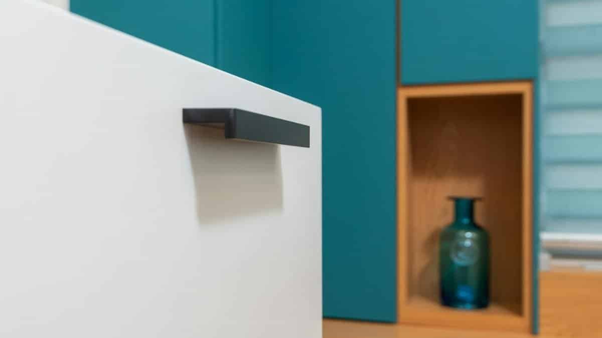 Sleek minimalist kitchen design with teal cabinets and decorative vase.