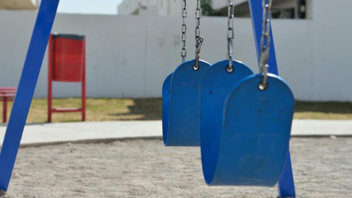 Blue swings in a sunny outdoor playground with sand and grass.