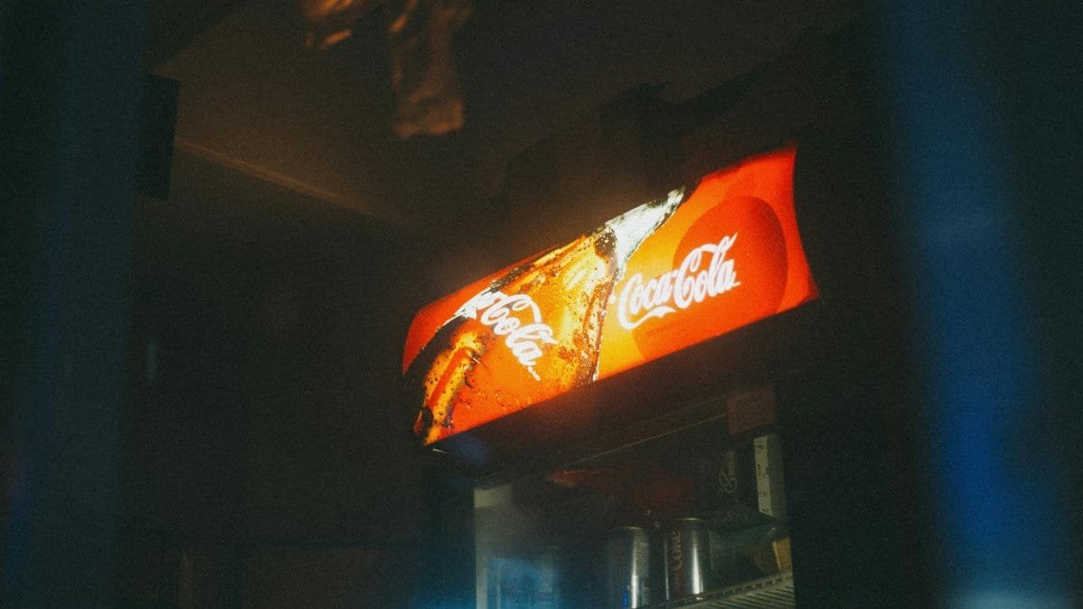 A Coca-Cola cooler illuminated in low light with a vintage aesthetic, displaying iconic branding.