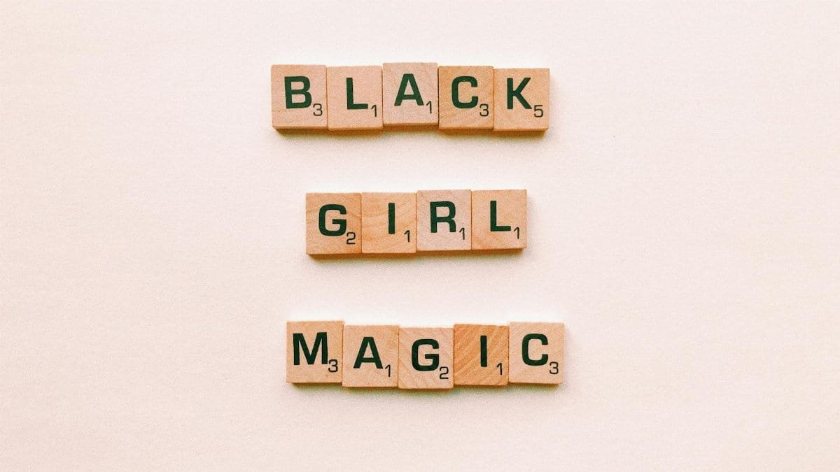Wooden Scrabble tiles spell out 'Black Girl Magic' on a soft neutral background, emphasizing empowerment.