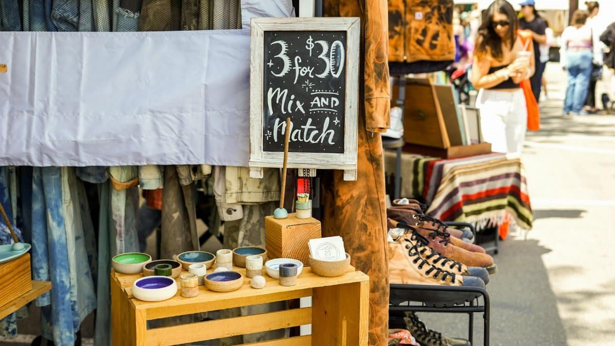 A vibrant street market stall displaying clothes, pottery, and more with a mix-and-match offer sign.