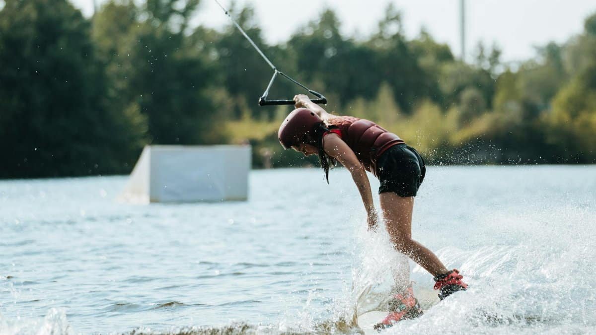 An adult woman skillfully wakeboarding on a sunny day, splashing water with her movements.