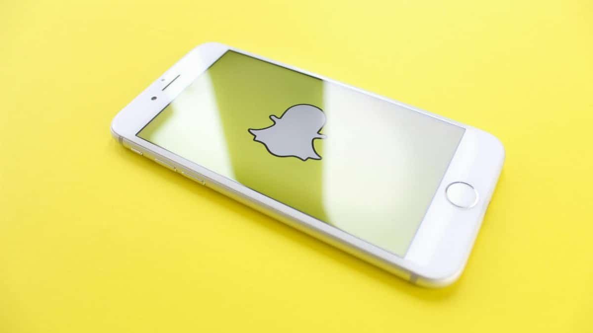 White smartphone displaying Snapchat logo on a bright yellow background, angled view.