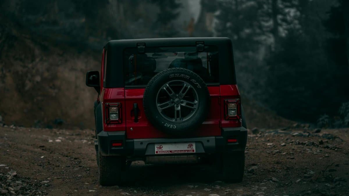 A red off-road vehicle travels down a rugged dirt path surrounded by forest scenery, perfect for adventure seekers.
