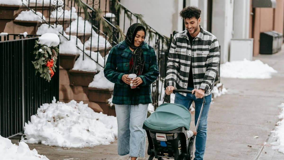 A joyful couple strolling with a baby stroller on a snowy city sidewalk.