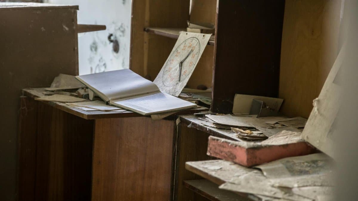 A cluttered, dusty office with open books, papers, and shelves, evoking a rustic and abandoned feel.