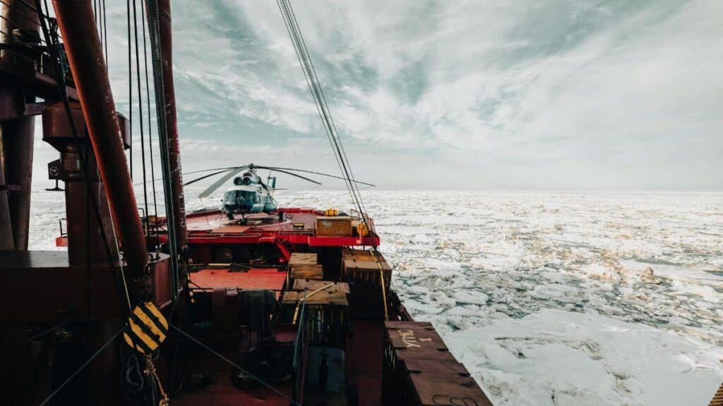 A helicopter on the deck of an icebreaker ship navigating through icy Arctic waters.