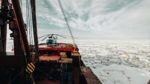 A helicopter on the deck of an icebreaker ship navigating through icy Arctic waters.