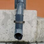 Aged metal drain pipe on a concrete wall with water stains, highlighting urban decay.