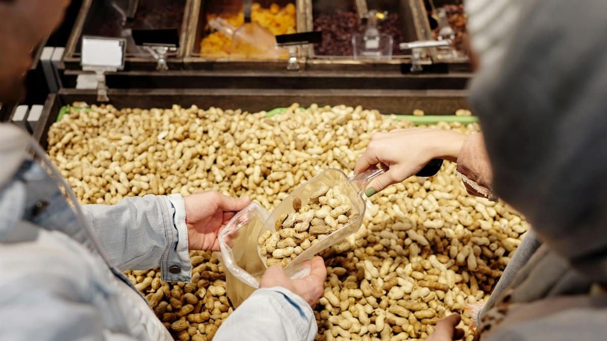 Two people buying peanuts in a supermarket using a scoop. Fresh and bulk food concept.