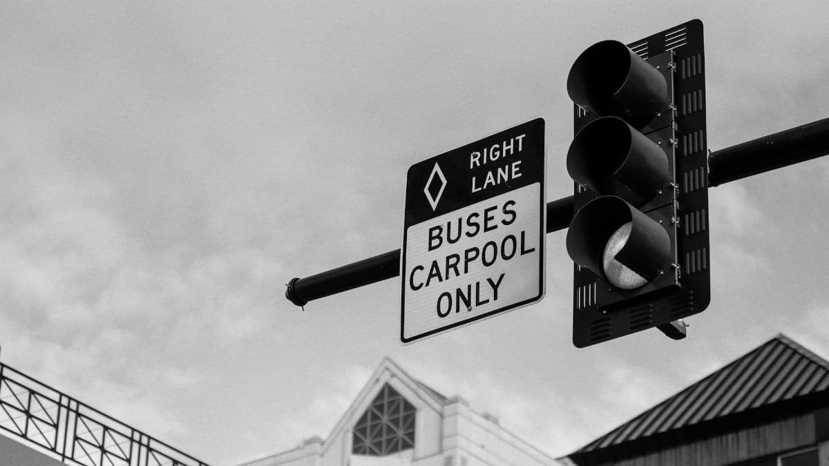 Black and white photo of a traffic signal with 'Buses Carpool Only' sign, showing urban architecture.