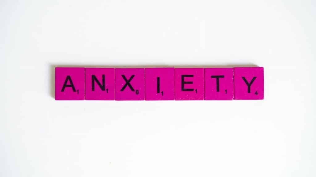 Pink Scrabble tiles spelling 'anxiety' on a white surface. Concept of mental health.