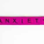Pink Scrabble tiles spelling 'anxiety' on a white surface. Concept of mental health.