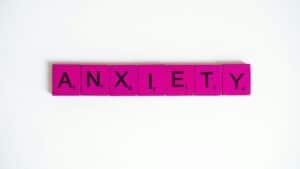 Pink Scrabble tiles spelling 'anxiety' on a white surface. Concept of mental health.