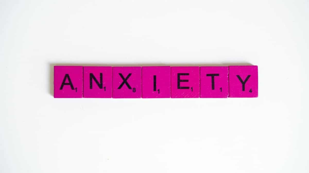 Pink Scrabble tiles spelling 'anxiety' on a white surface. Concept of mental health.