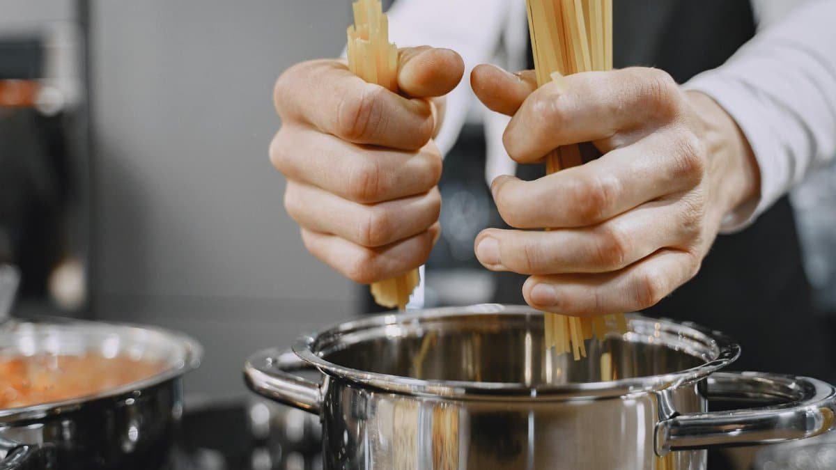 Close-up of chef's hands adding pasta to a boiling pot in a kitchen.