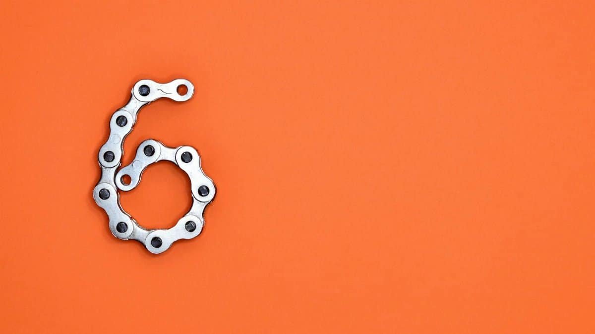 A creative display of a bike chain forming the number six against a vibrant orange backdrop.