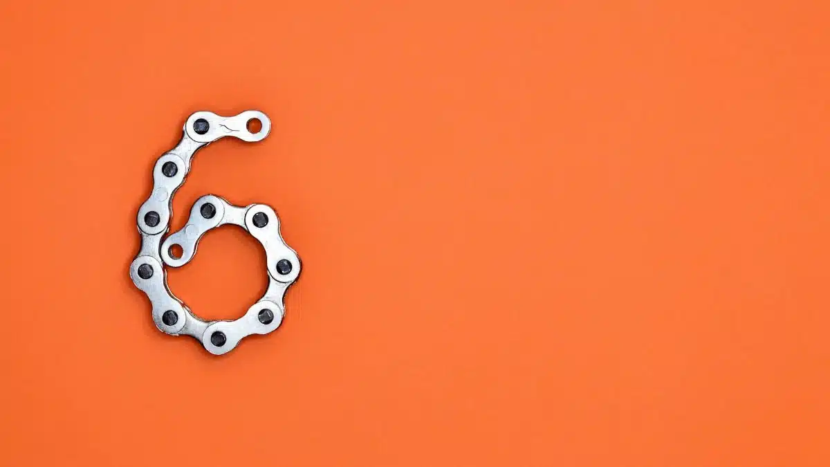 A creative display of a bike chain forming the number six against a vibrant orange backdrop.