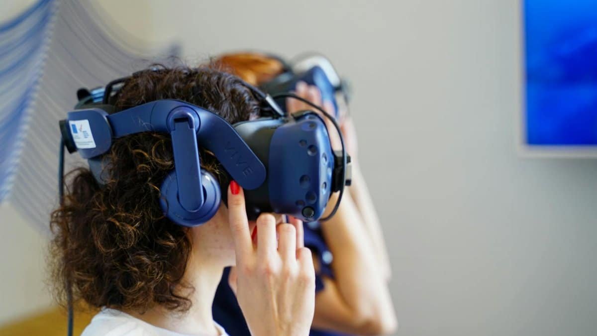 Two women using VR headsets, fully immersed in virtual reality technology indoors.