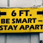 Yellow sign urging social distancing with 'Be Smart, Stay Apart' message on wood.