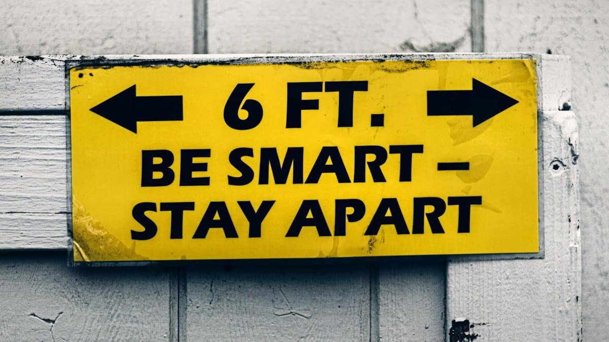 Yellow sign urging social distancing with 'Be Smart, Stay Apart' message on wood.