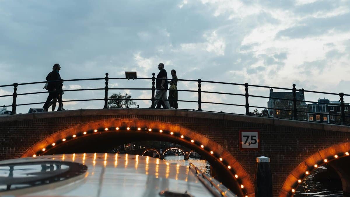 Scenic evening view of people walking over a lit bridge in Amsterdam, capturing the city's urban charm.