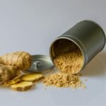 Close-up of fresh ginger root with sliced pieces and ginger powder spilled from a metal container.