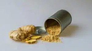 Close-up of fresh ginger root with sliced pieces and ginger powder spilled from a metal container.