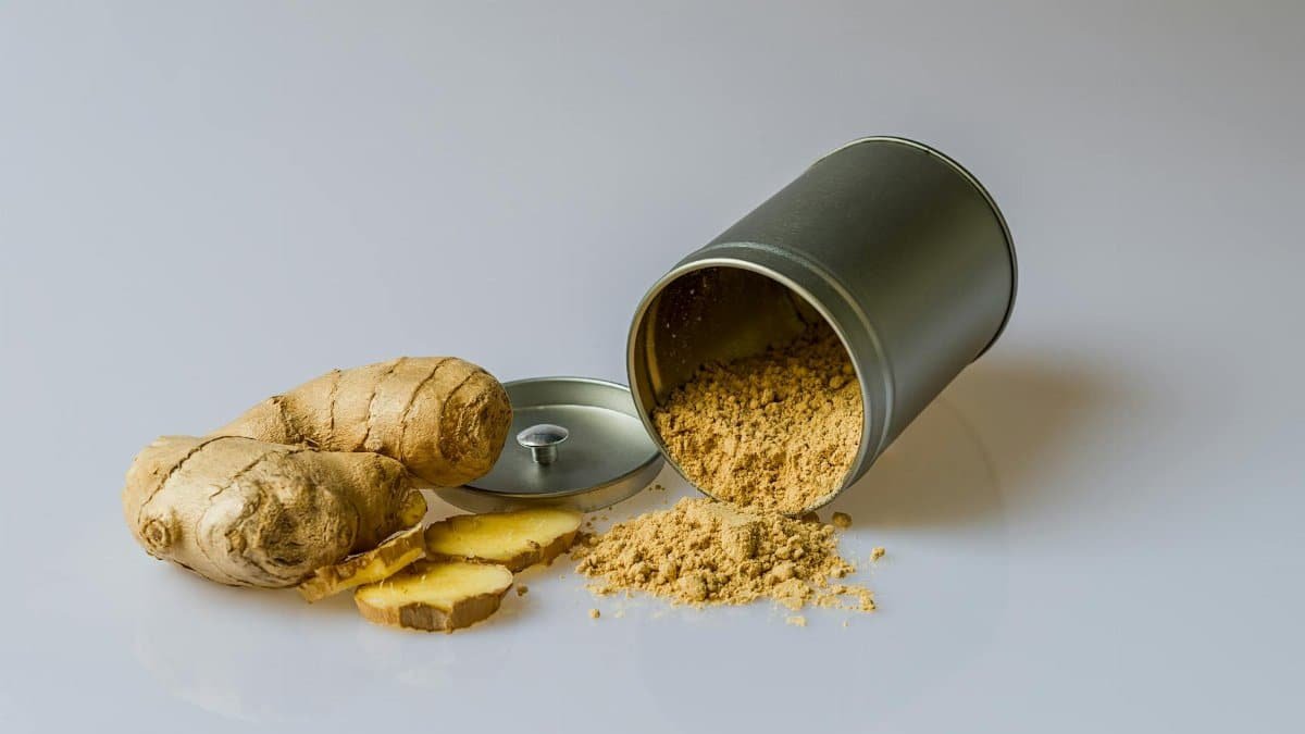 Close-up of fresh ginger root with sliced pieces and ginger powder spilled from a metal container.