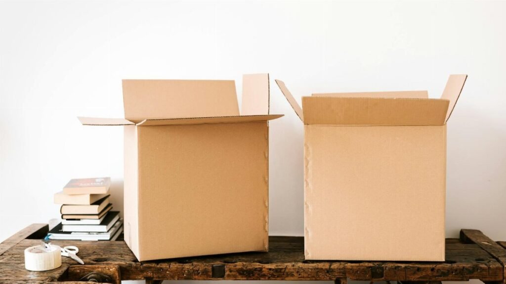 Opened carton boxes and stacked books placed on shabby wooden desk with tape against white wall