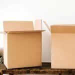 Opened carton boxes and stacked books placed on shabby wooden desk with tape against white wall